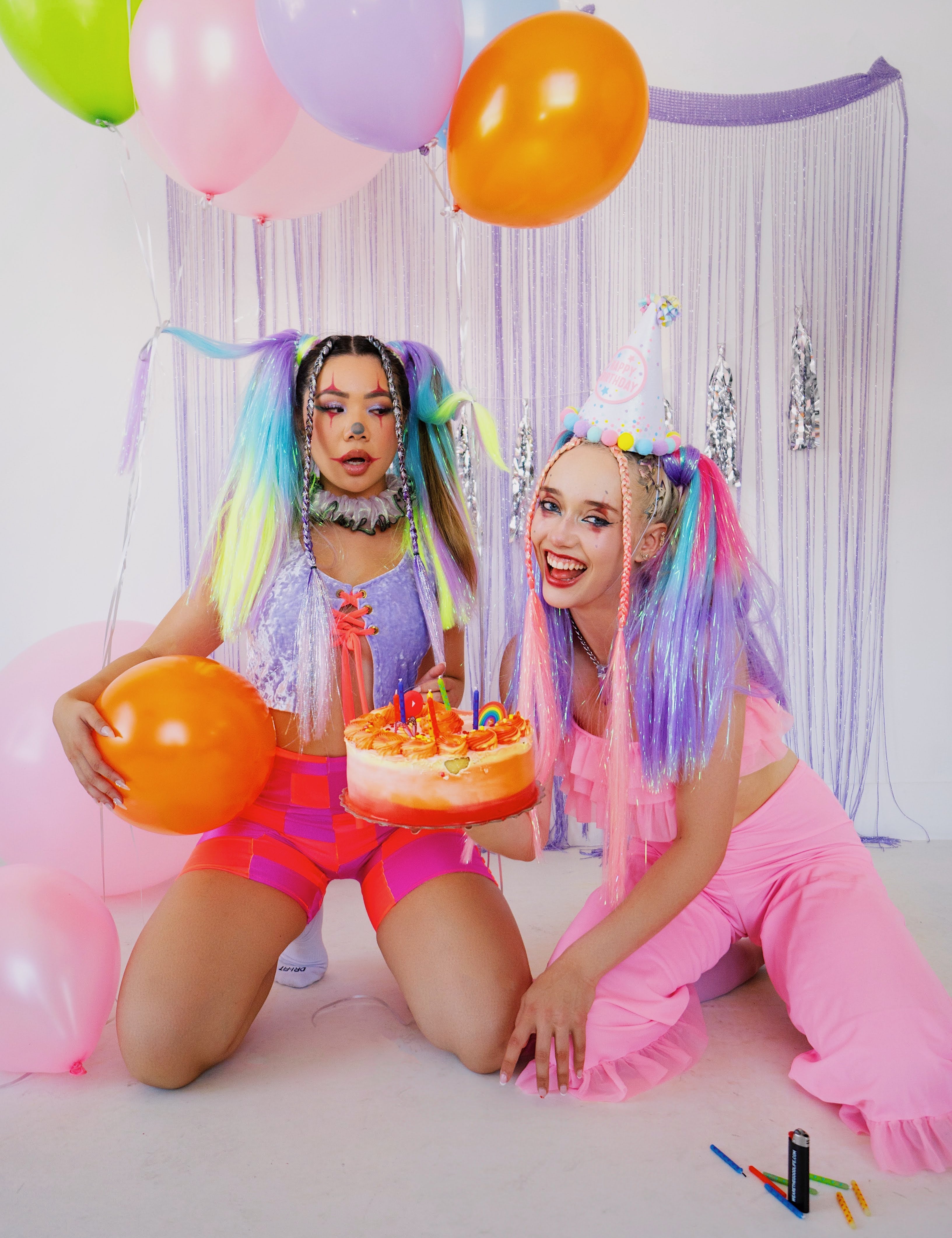 2 women dressed as clowns holding a balloon and cake