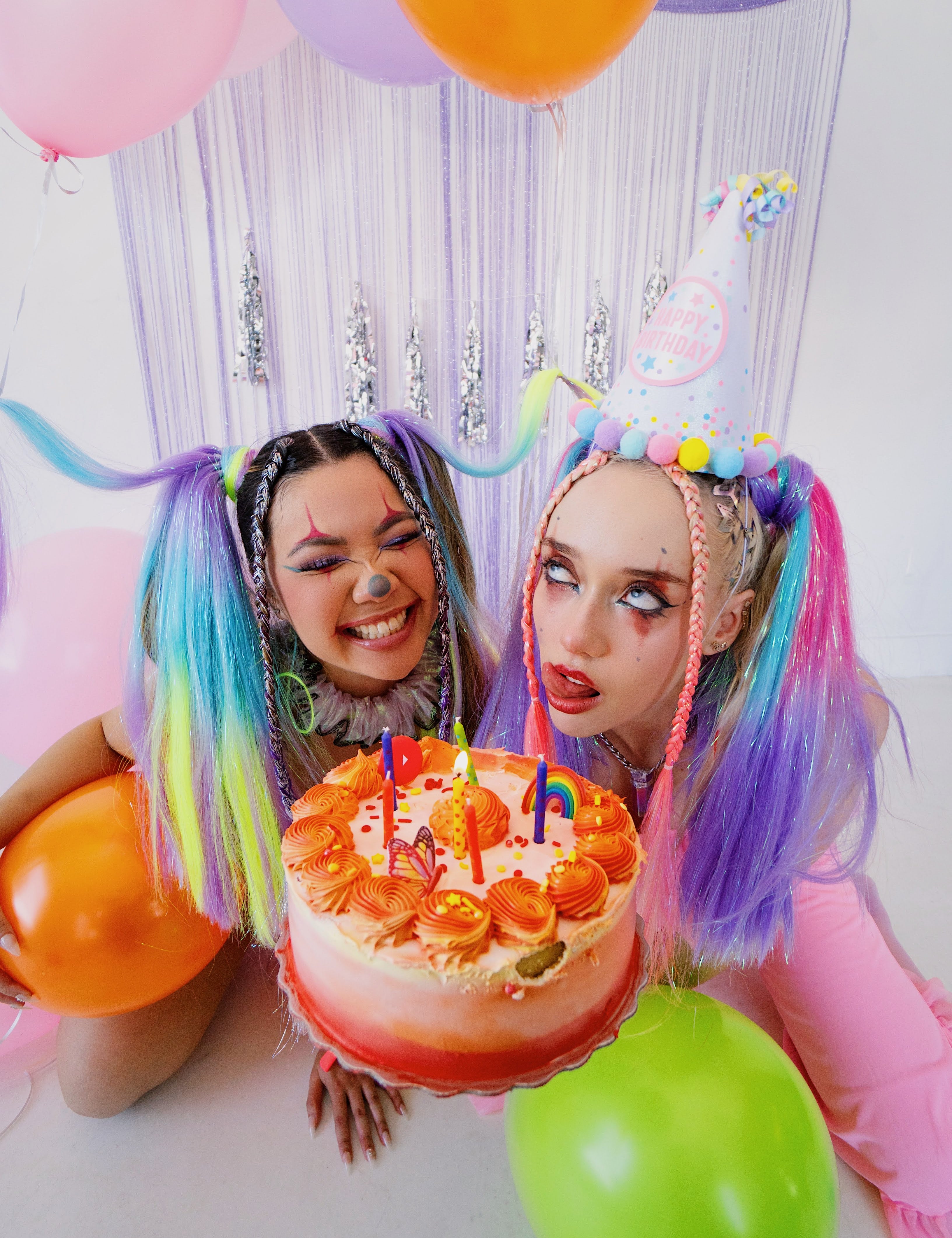 2 women in birthday rave attire holding a cake